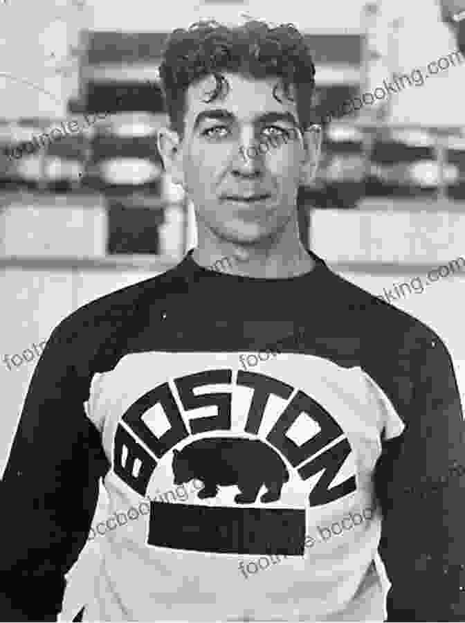 Lionel Hitchman, A Boston Bruins Legend, Stands On The Ice With His Hockey Stick Raised In The Air. He Is Wearing A Bruins Jersey And A Helmet. His Face Is Obscured By The Visor On His Helmet, But His Eyes Are Visible And They Are Full Of Determination. The Image Is Taken From A Black And White Photograph. Hitch Hockey S Unsung Hero: The Story Of Boston Bruin Lionel Hitchman